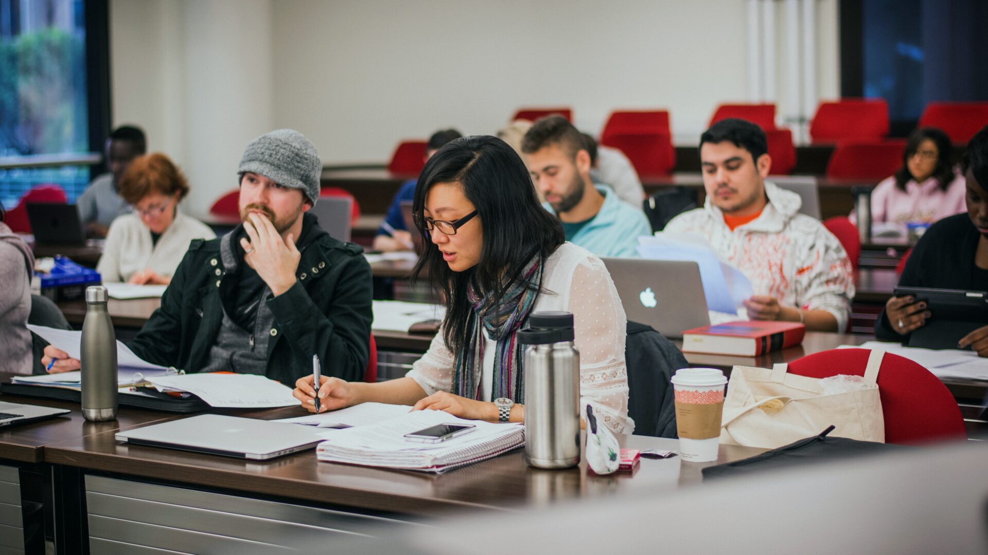 Students sit in a classroom, taking notes and working on computers.