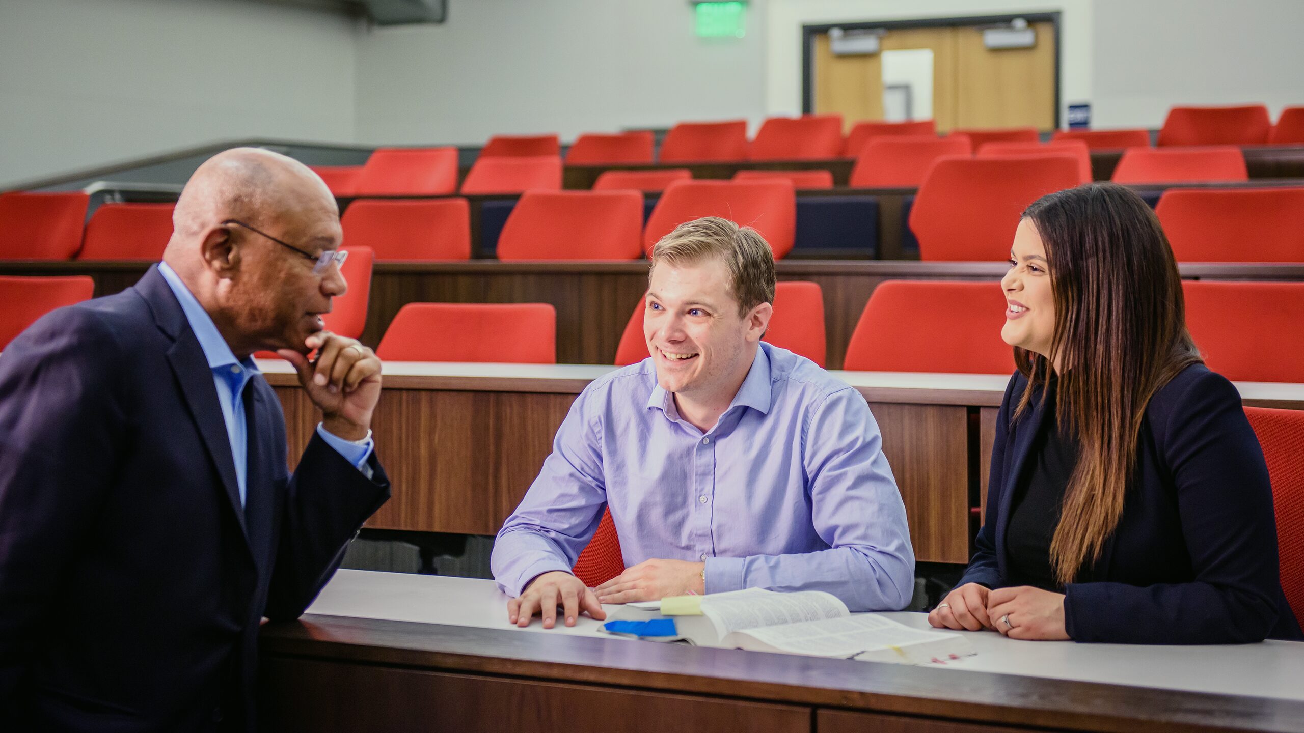 Two students talking with a professor in a classroom.